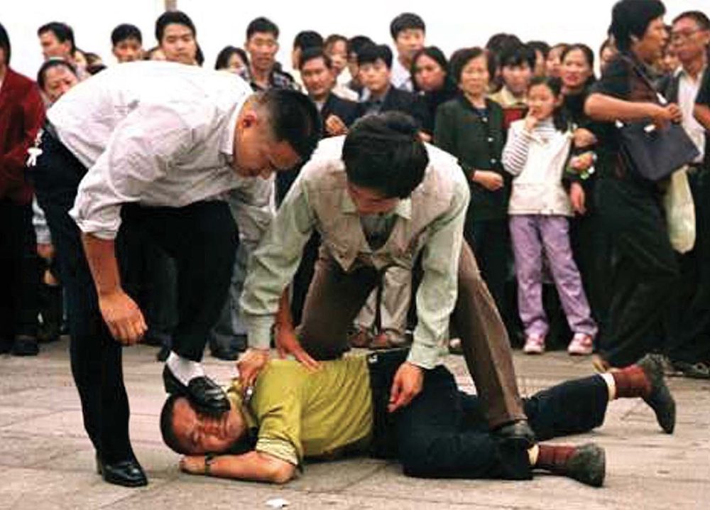 Plainclothes police officers pinning a Falun Gong practitioner to the ground in Beijing as a crowd watches