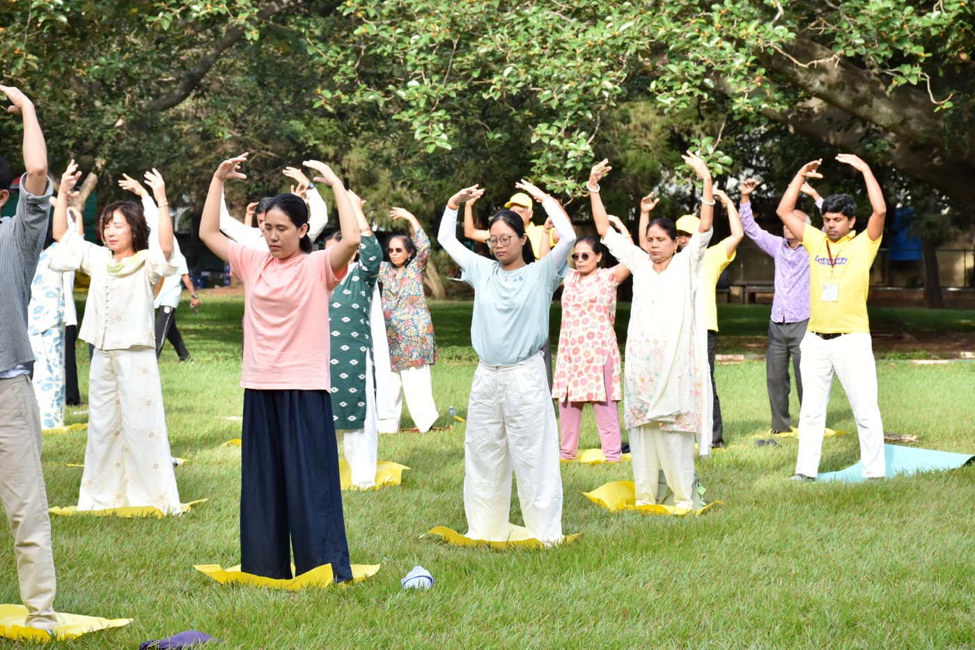 Practitioners with arms raised in the second Falun Dafa exercise under park trees