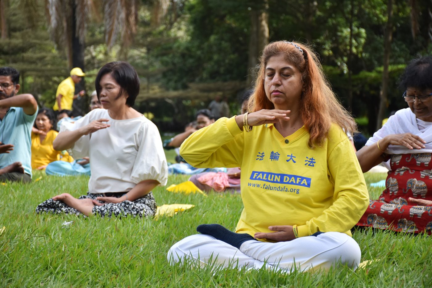Practitioner in a Falun Dafa shirt meditating cross-legged in a park